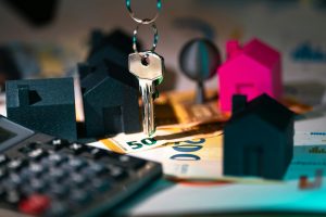 calculator, miniature houses, and banknotes under a dangling key
